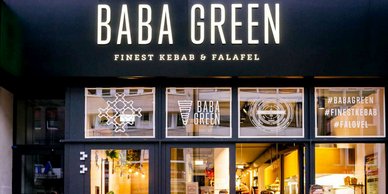Das Restaurant 'Baba Green' bietet eine einladende Fassade mit großen Fenstern und einem modernen, stilvollen Design.