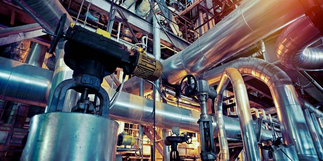 Ein komplexes Netzwerk aus glänzenden Metallrohren und Maschinen in einer industriellen Umgebung, beleuchtet von warmem Licht.