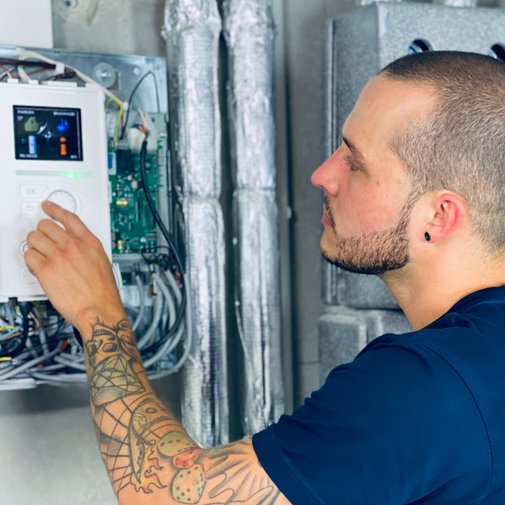 Techniker programmiert moderne Steuerungseinheit mit Präzision Ein Mann mit Tattoos arbeitet konzentriert an einem Steuergerät, während er einen Knopf drückt und auf den Bildschirm schaut.