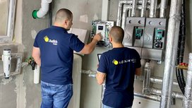 Zwei Techniker in blauen T-Shirts arbeiten an einer Steuerungseinheit, um die Heizungsanlage zu überprüfen und einzustellen.
