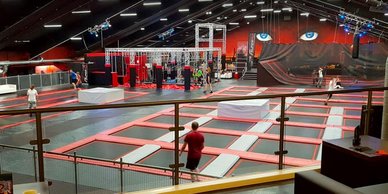 Eine große Trampolinhalle mit mehreren Trampolinen, in der Menschen aktiv springen und spielen.
