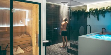 Ein Mann steht unter einer Regendusche in einem modernen Wellnessbereich, während eine Frau in einem Whirlpool entspannt.
