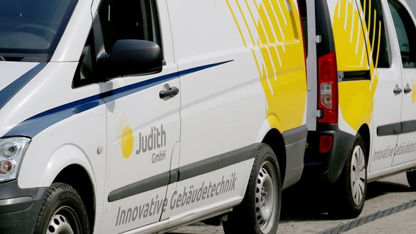 Zwei Lieferwagen stehen nebeneinander, einer mit gelbem Design und der Aufschrift 'Judith GmbH' auf der Seite.