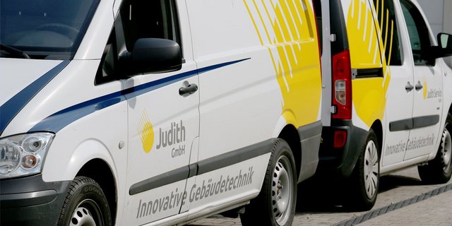 Zwei Lieferwagen stehen nebeneinander, einer mit gelbem Design und der Aufschrift 'Judith GmbH' auf der Seite.