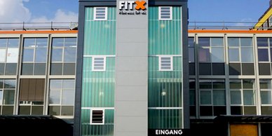 Das moderne Fitnessstudio mit dem Namen FITX hat eine große Glasfassade und einen klaren blauen Himmel im Hintergrund.