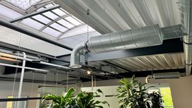 Ein moderner Raum mit sichtbaren Lüftungsrohren und Pflanzen, die eine grüne Note in die industrielle Umgebung bringen.