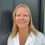 Lächelnde Frau vor modernem Hintergrund in Weiß Eine lächelnde Frau mit blonden Haaren trägt eine weiße Bluse und steht vor einer modernen, dunklen Wand.