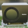 Moderne Wärmepumpe im Garten für nachhaltige Energie Eine schwarze Wärmepumpe steht auf einem grauen Fundament, umgeben von grünem Gras und kleinen Steinen.