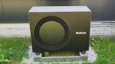 Moderne Wärmepumpe im Garten für nachhaltige Energie Eine schwarze Wärmepumpe steht auf einem grauen Fundament, umgeben von grünem Gras und kleinen Steinen.