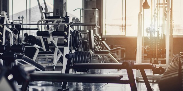 Ein modernes Fitnessstudio mit verschiedenen Trainingsgeräten und Hanteln, beleuchtet von natürlichem Licht durch große Fenster.
